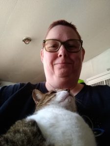 Selfie of me (middle aged woman) holding a tabby and white cat in her lap. Cat looks content.